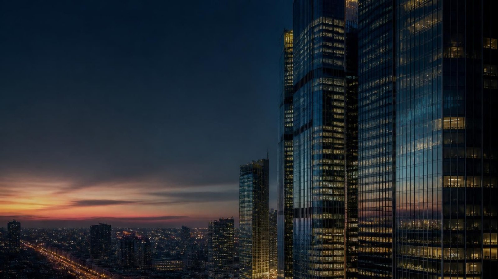 Glass towers in a financial district at dusk, with open sky on the left and no readable signage